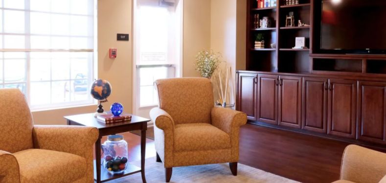 A cozy living room with an armchair, a small table with decorations, and a bookshelf.