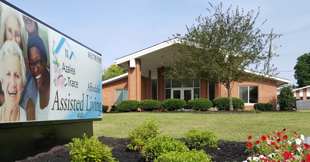 A brick building with a sign indicating it is an assisted living facility, surrounded by landscaping.