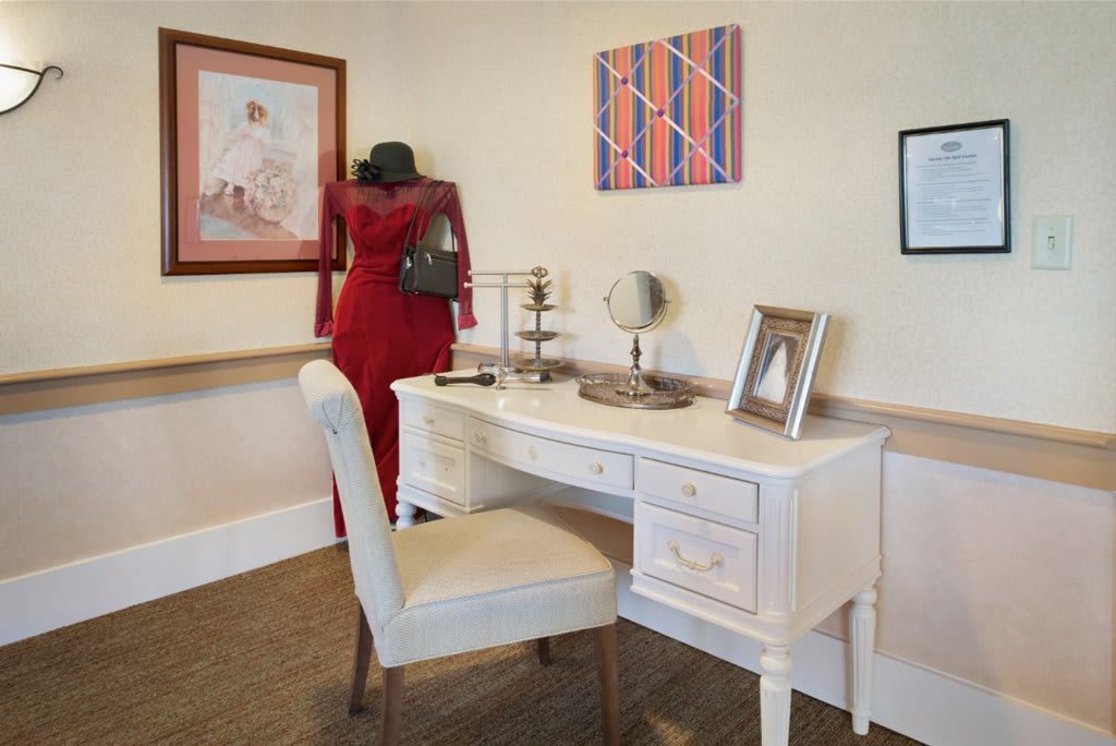 A cozy interior scene with a white desk and chair, decorated with artwork on the walls and a woman in red observing a painting.