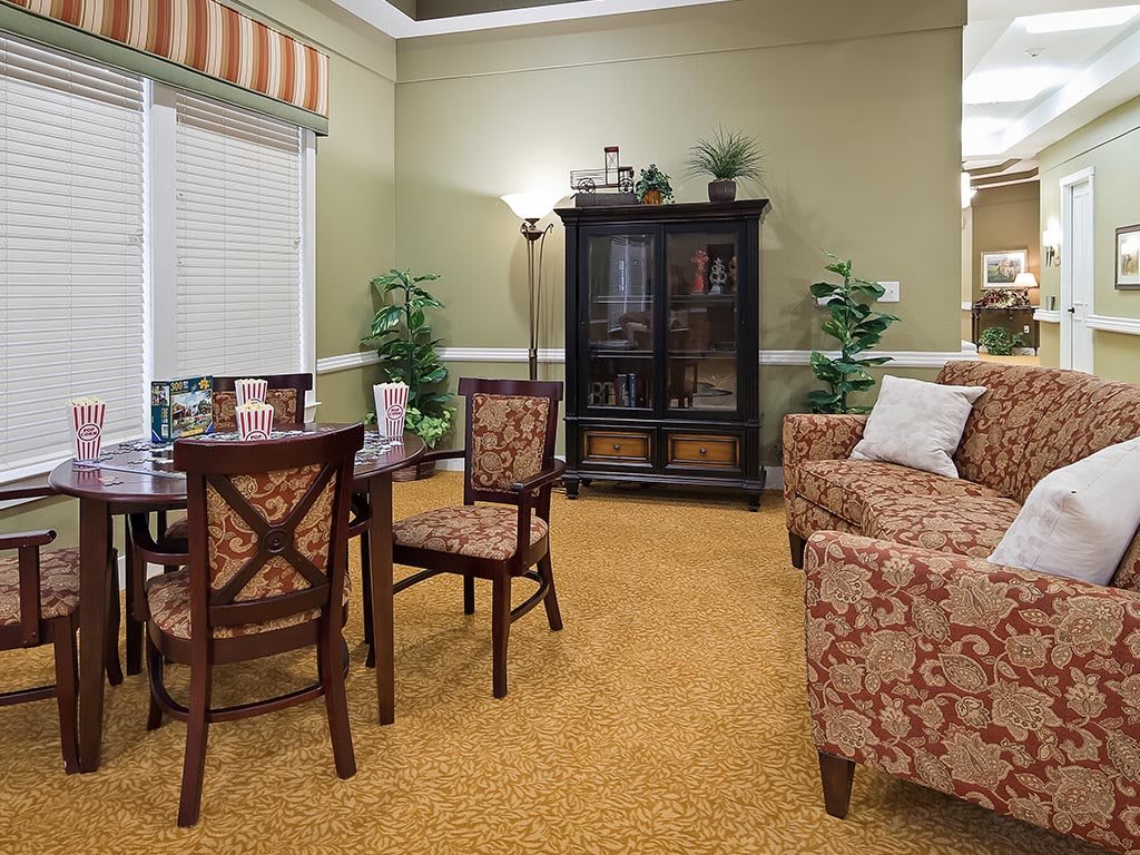 A cozy living room featuring patterned furniture, a dark cabinet, and indoor plants.