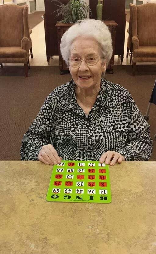 An elderly woman smiles while playing a game of bingo indoors.