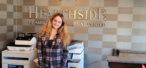 A young woman smiling in front of a printer at a nursing center.