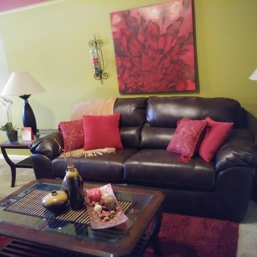 A cozy living room featuring a dark leather sofa with red cushions, a coffee table decorated with ornaments, and warm lighting.