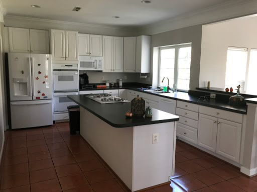 A spacious and modern kitchen featuring white cabinetry and black countertops, illuminated by natural light.
