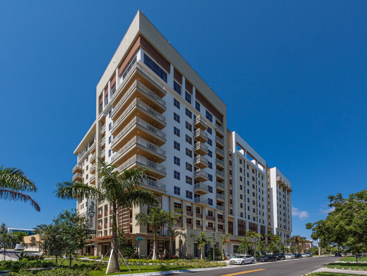 A modern high-rise apartment building with palm trees lining the street.