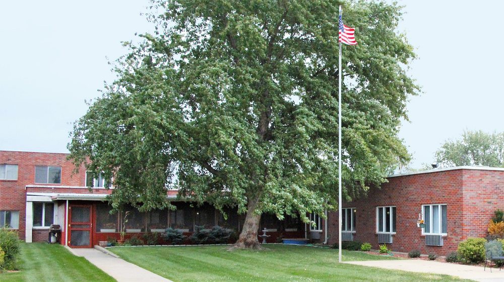 A brick building with a large tree and an American flag on a lawn.