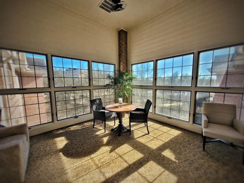 A sunlit room with large windows, featuring a table and chairs alongside a potted plant.