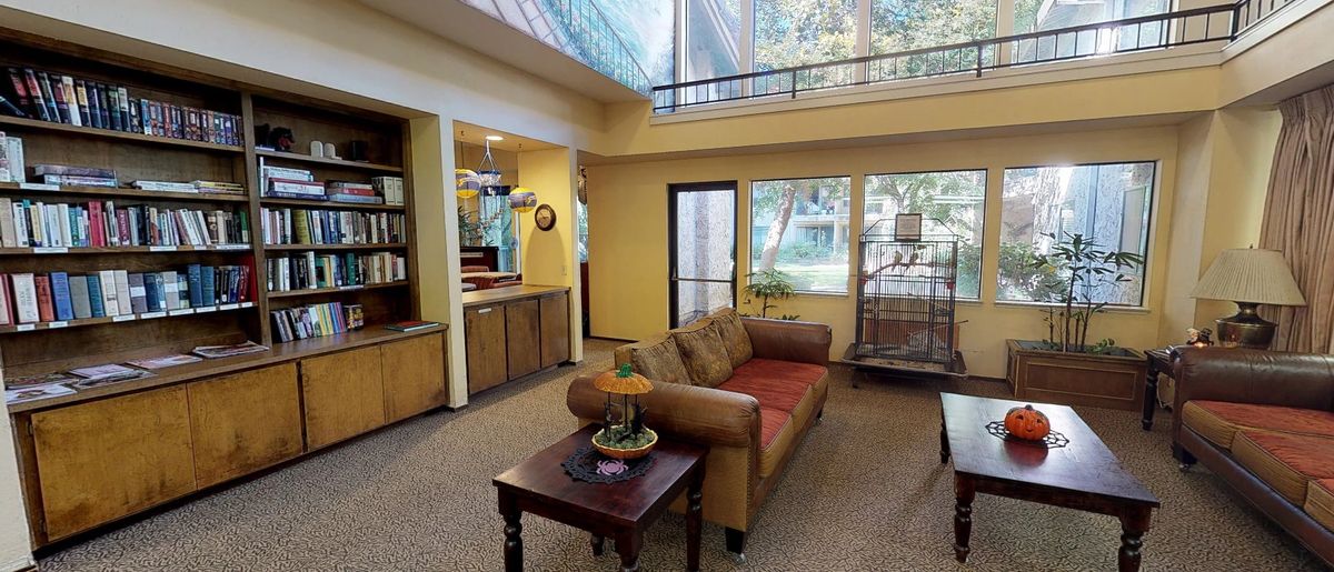 A cozy living room with a sofa, coffee table, bookshelf, and large windows.