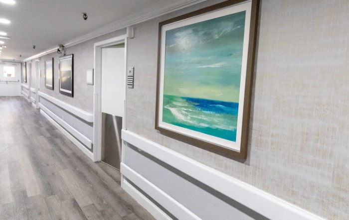 A hallway featuring a framed painting of an ocean scene on the wall.