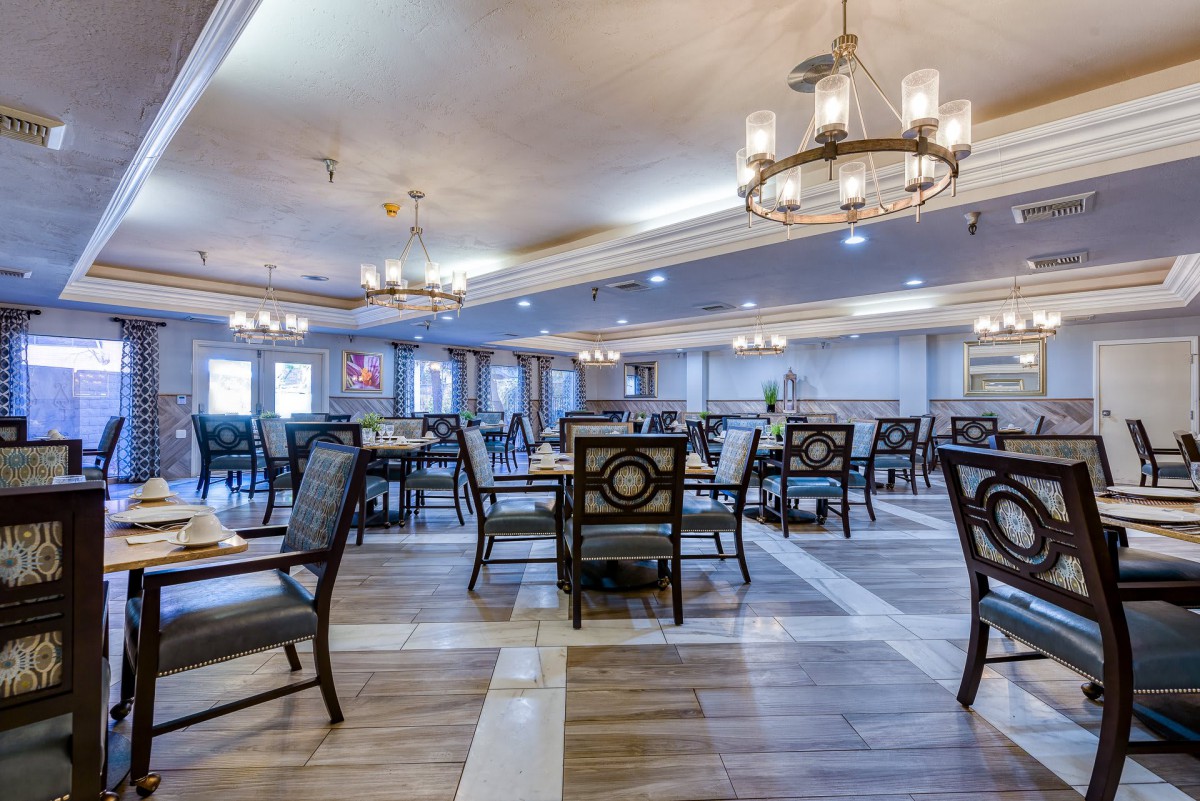 A spacious dining room with elegant chandeliers, neatly arranged tables and chairs.