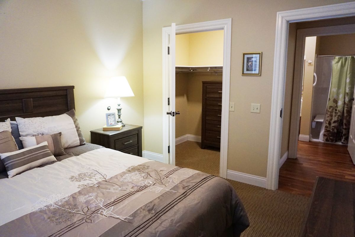A cozy bedroom with a neatly made bed, bedside lamp, and an open closet door.