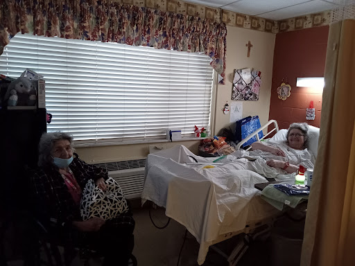 A hospital room with a patient in bed and a visitor seated nearby.