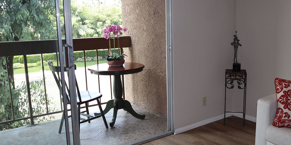 A cozy balcony corner featuring a small round table with an orchid plant, accompanied by a wooden chair.
