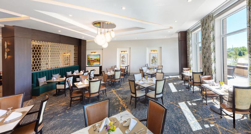 An elegantly designed dining room with neatly arranged tables and chairs, featuring modern chandeliers and decorative artwork on the walls.