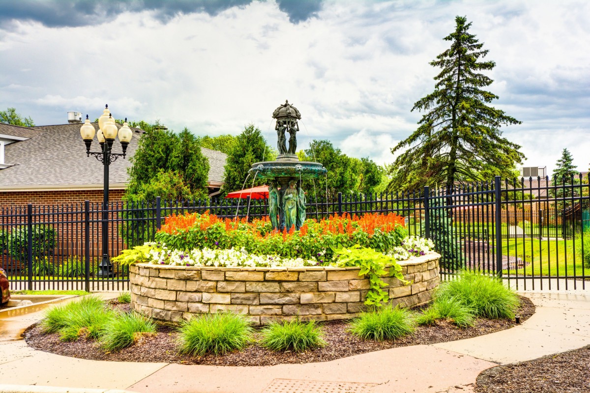 A beautifully landscaped garden with a stone wall and fountain centerpiece, surrounded by vibrant flowers and lush greenery.