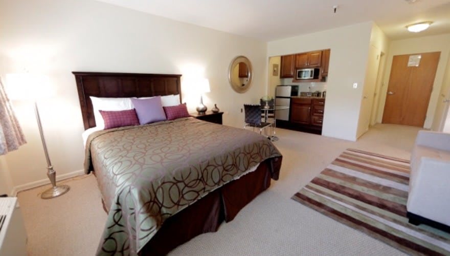 A cozy bedroom with an adjoining kitchenette, featuring a large bed and decorative elements like a mirror and lamp.
