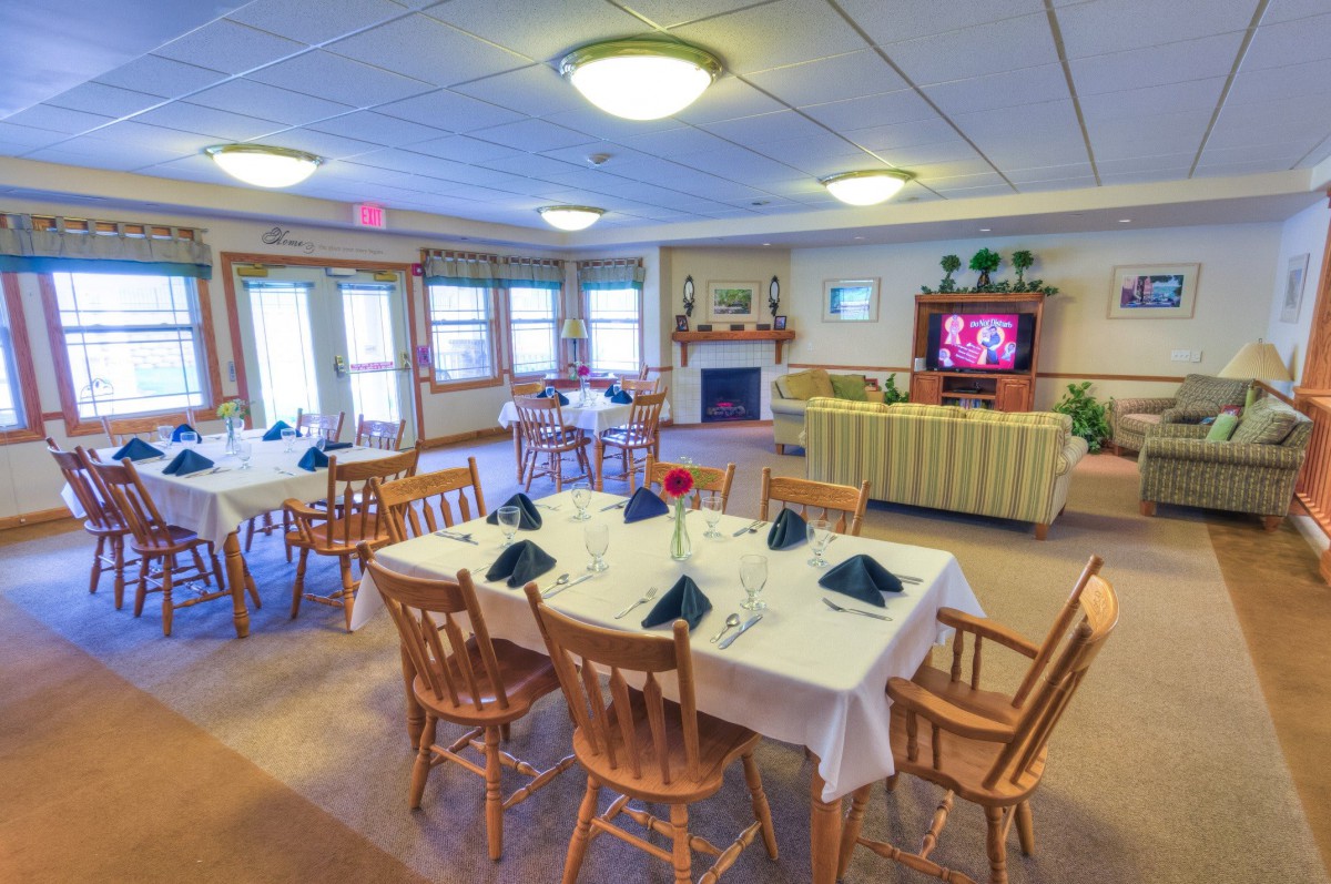 A cozy dining area with neatly arranged tables, chairs, and a fireplace, complemented by a television for entertainment.