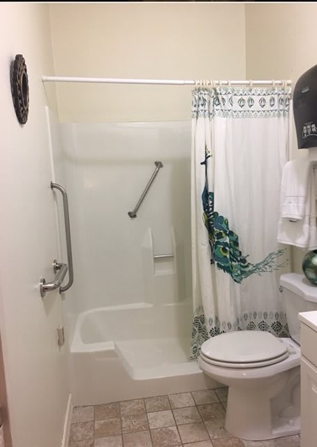A bathroom featuring a shower-tub combo with a decorative curtain, toilet, and safety grab bar.