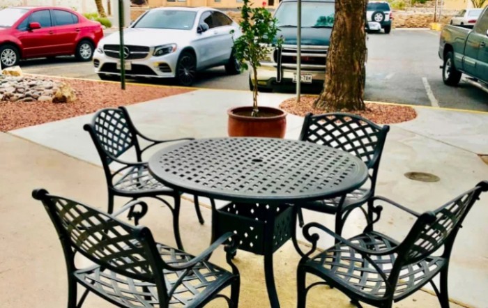 An outdoor patio set with a round table and four chairs near a parking lot, accompanied by a potted plant.