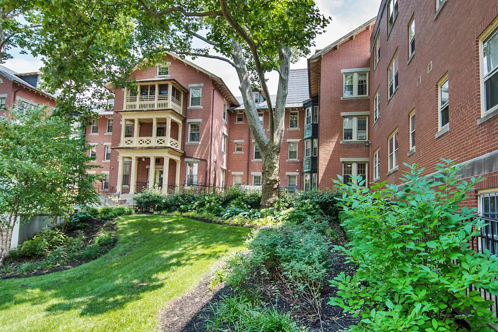 Brick residential building surrounded by lush greenery and landscaping.