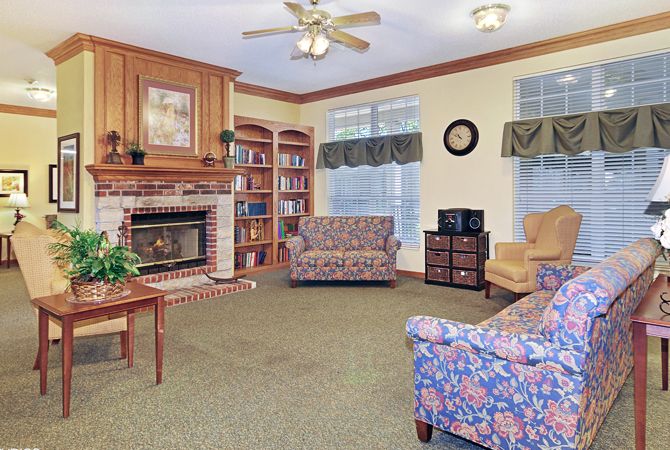 A cozy living room featuring a brick fireplace, bookshelves, and patterned armchairs.