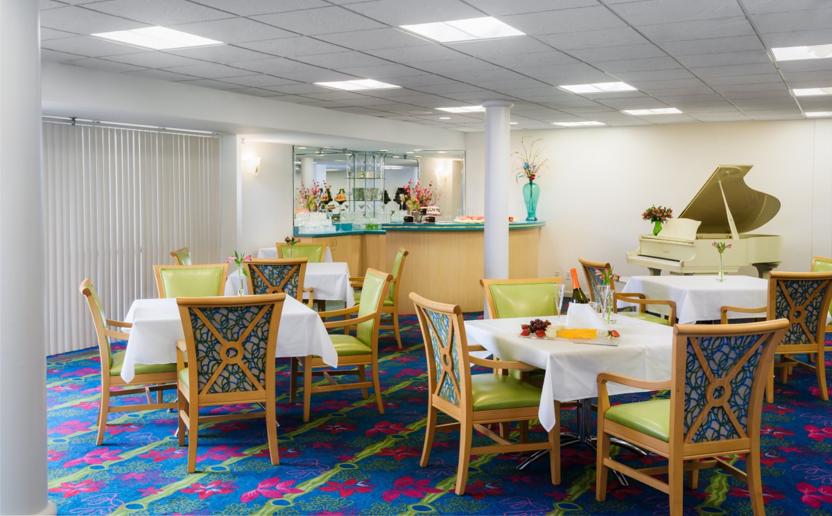 A well-lit dining area with neatly arranged tables and chairs, featuring colorful carpet and decor.