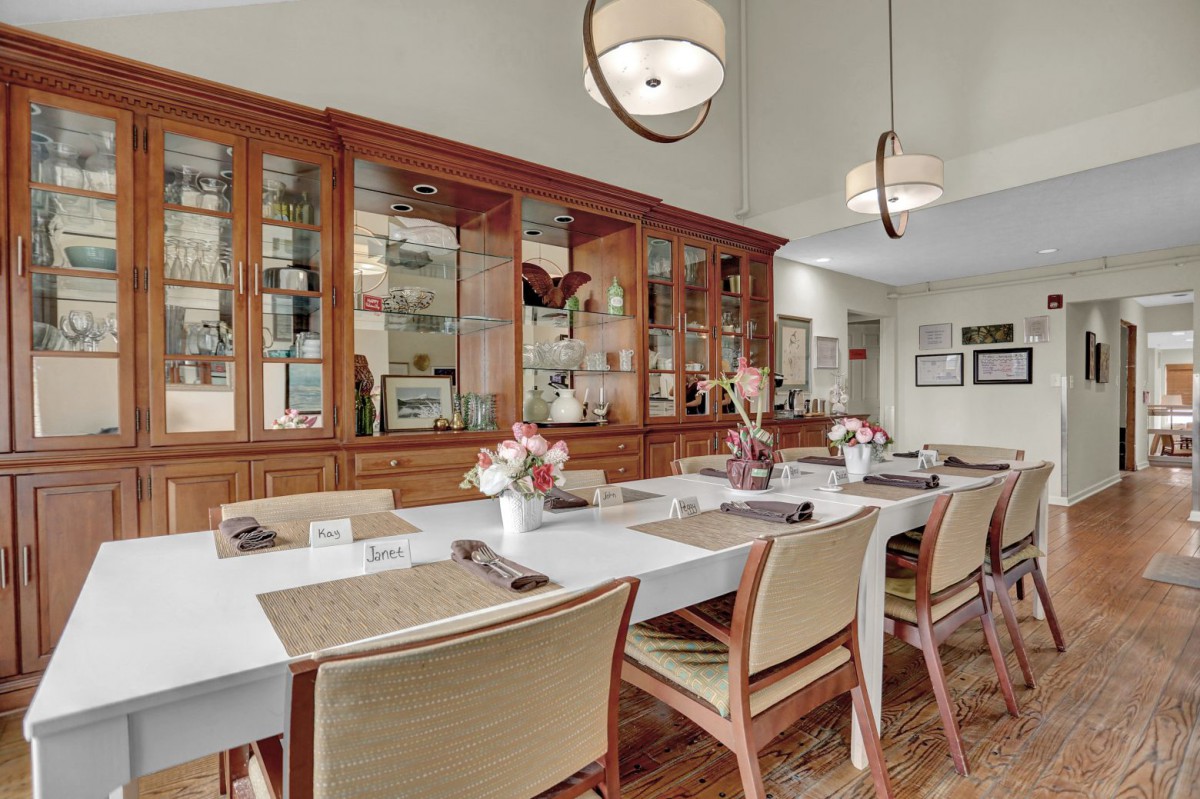 A modern dining room with a long table, stylish chairs, and wooden cabinets adorned with decor items.