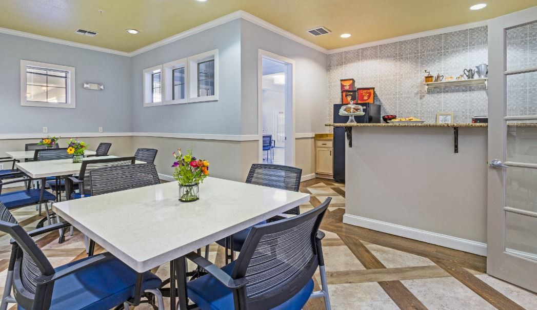 A modern dining area with a white table, black mesh chairs, and a small beverage station in the corner.