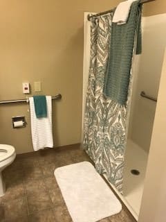 A bathroom featuring a toilet, a shower with a patterned curtain, and neatly hung towels.