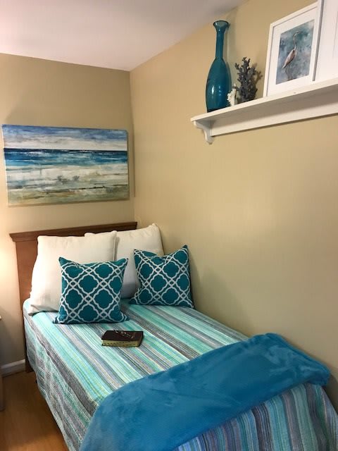 A cozy bedroom corner with beach-themed decor, featuring a neatly made bed and decorative pillows.