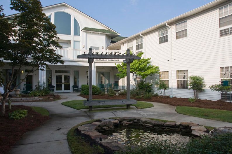 A peaceful courtyard garden with a pond and a pergola in front of a residential building.