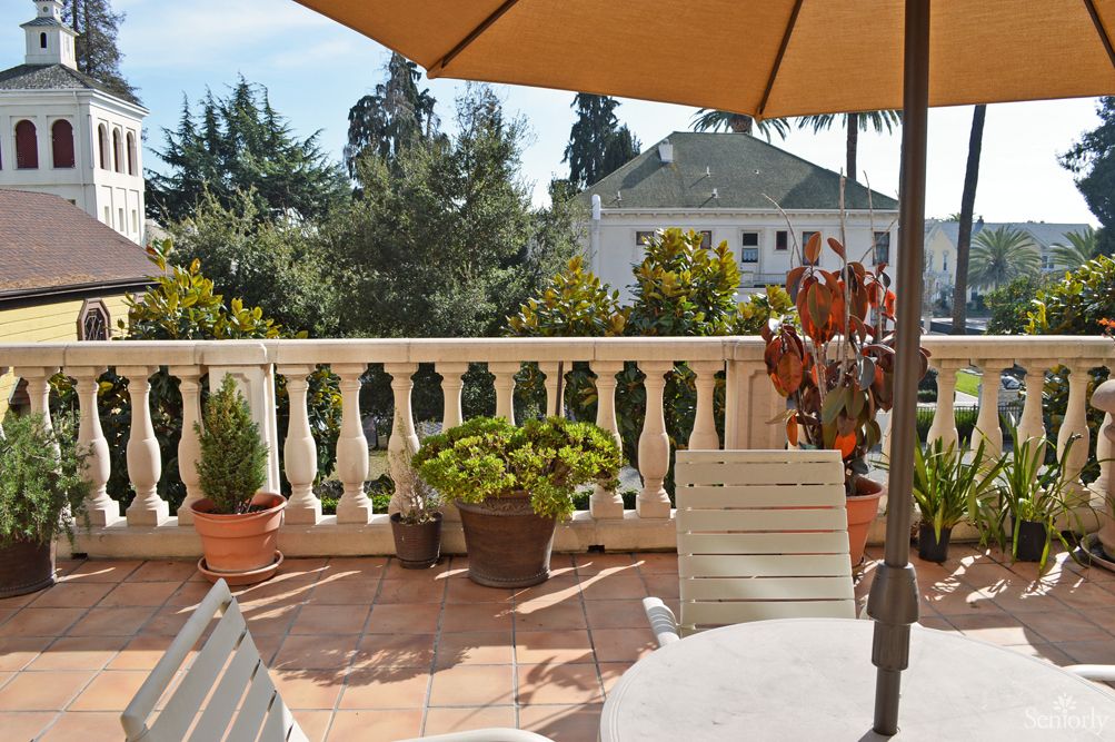 A sunny terrace with patio furniture, potted plants, and an umbrella.