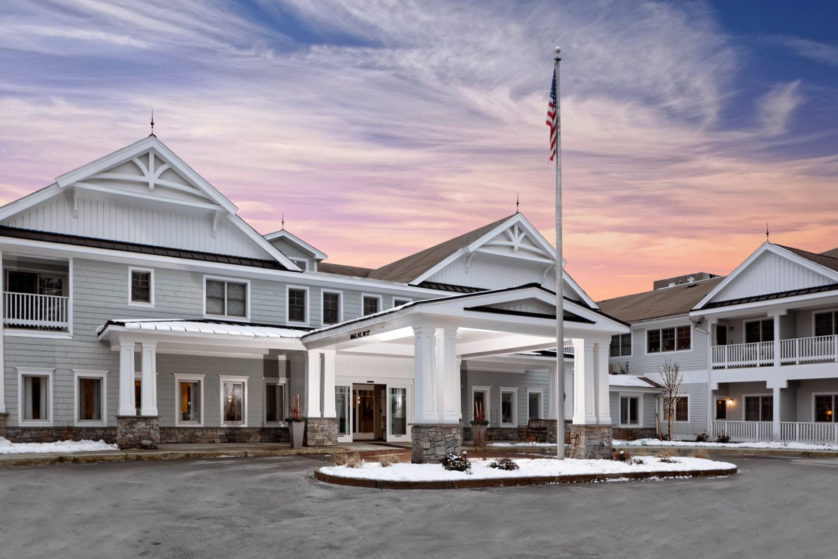 A large building with an elegant entrance at sunset, featuring an American flag and a picturesque sky.