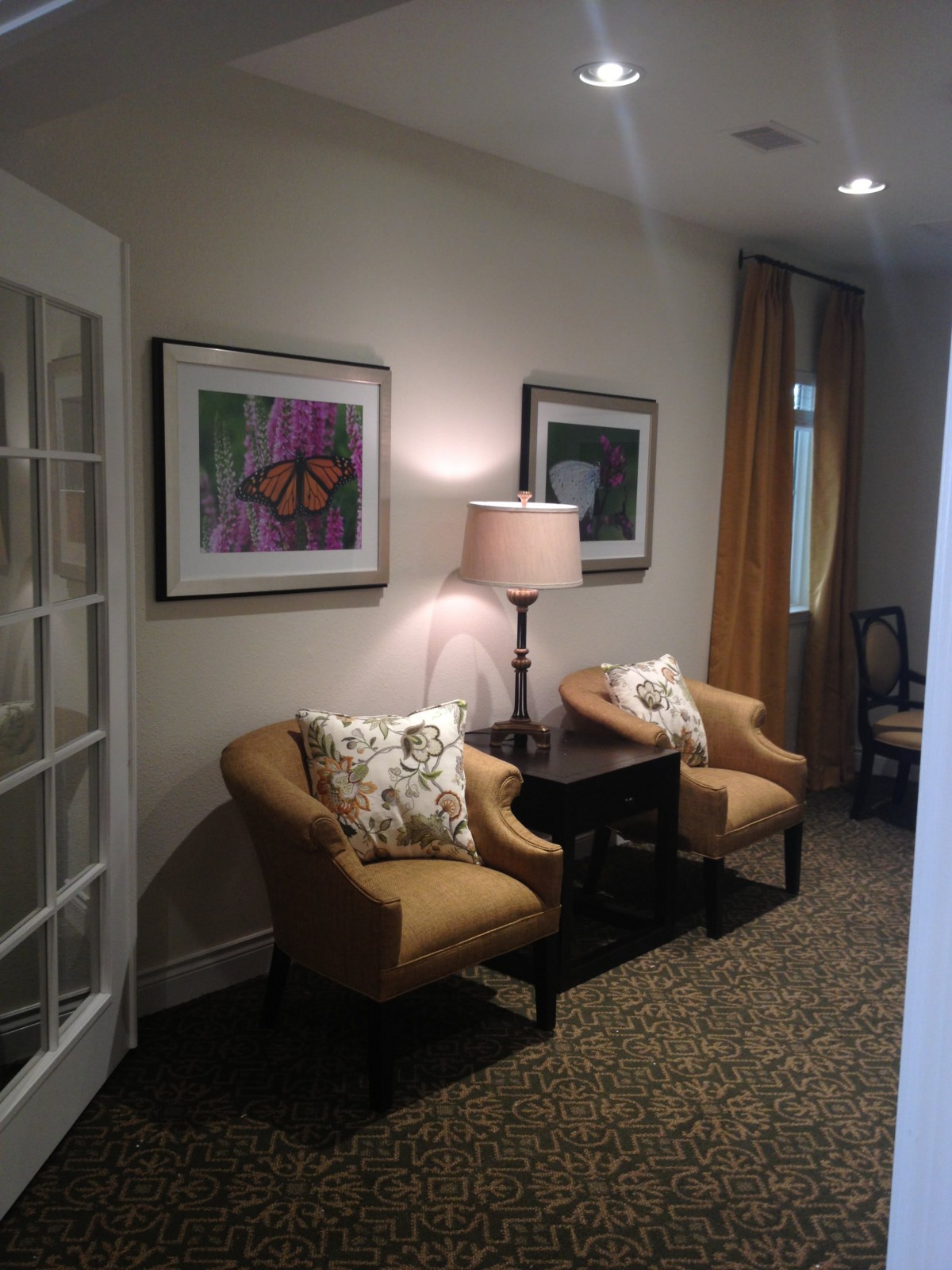 A cozy living area featuring two armchairs, a small table with a lamp, and framed artwork on the wall.