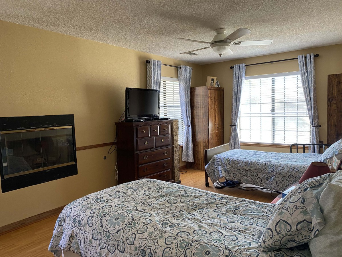 A cozy bedroom with two double beds, a TV on a dresser, and large windows allowing natural light.