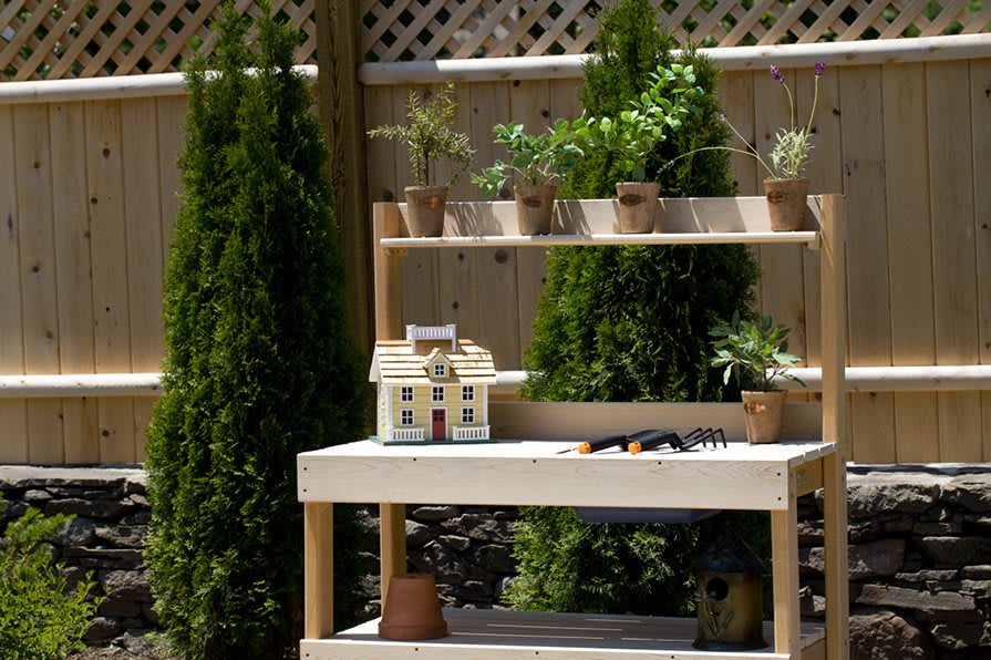 A garden potting bench with herbs and a miniature house model.