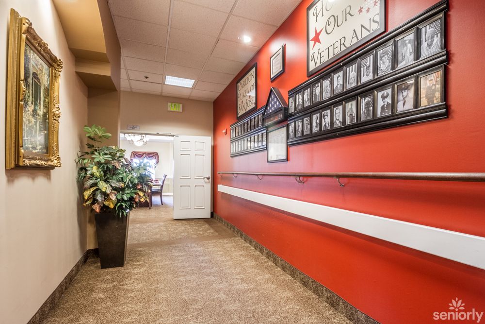 A hallway featuring a red wall adorned with framed pictures of veterans and a potted plant.