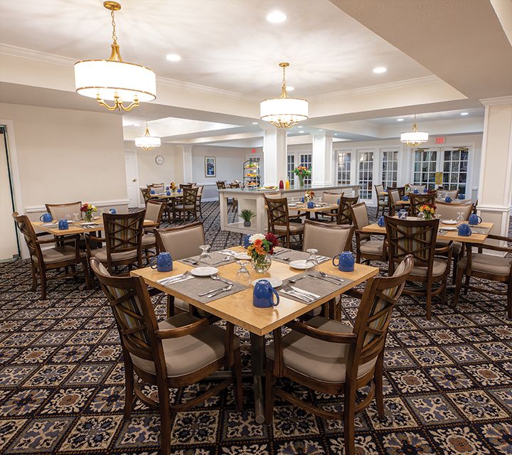 An elegant dining room with neatly arranged tables and chairs, featuring soft lighting.
