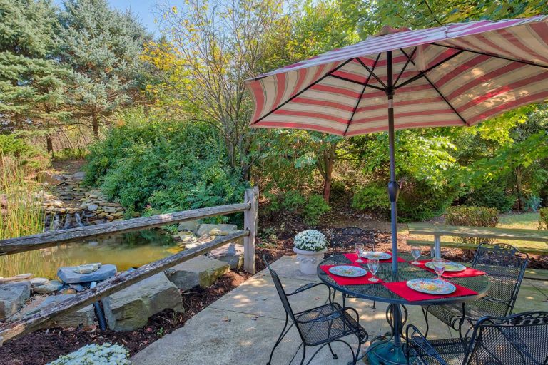 A cozy patio with a striped umbrella, set for dining amidst lush garden scenery.