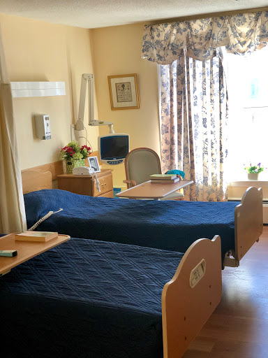 A serene hospital room featuring two patient beds, adorned with blue bedding, and bathed in natural light.