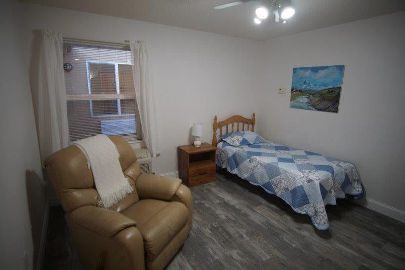 A cozy bedroom with a single bed, armchair, and a painting on the wall.