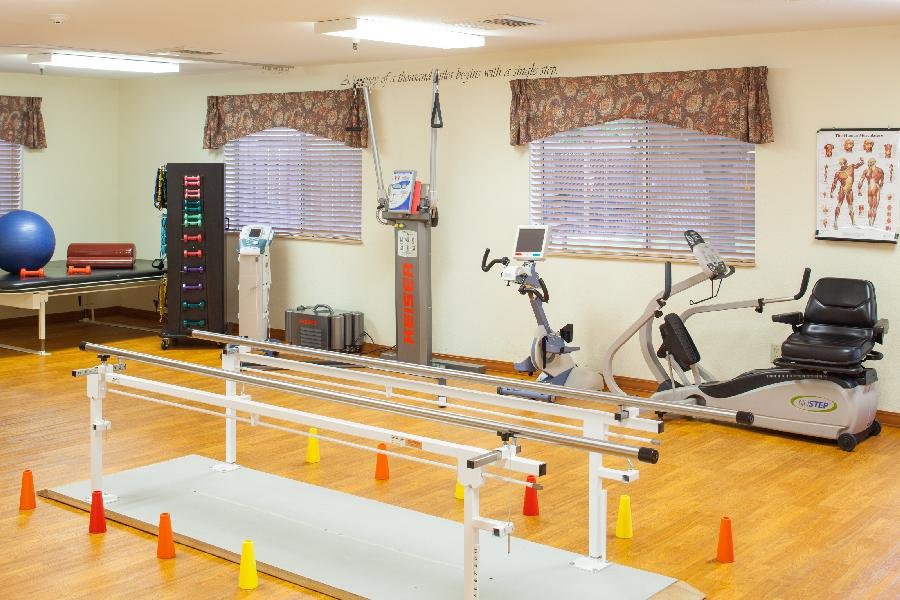 A rehabilitation room with exercise equipment including parallel bars and stationary bikes.
