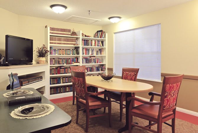 A cozy reading room with bookshelves, a round table, and comfortable chairs.