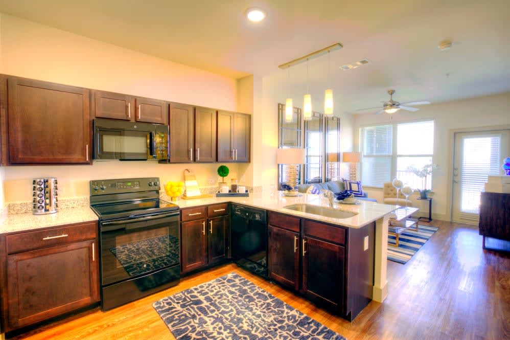 A modern kitchen with dark wooden cabinets and appliances in an open apartment layout.