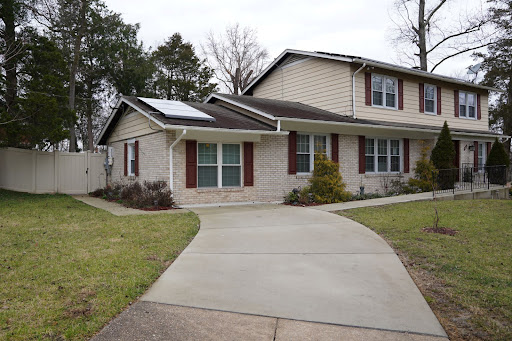 A charming two-story house featuring a well-maintained driveway and solar panels on the roof.