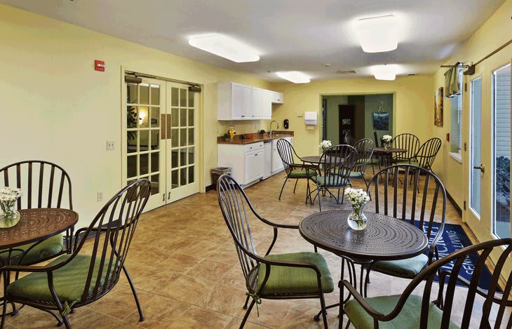 A cozy cafe with a modern design featuring several tables and chairs, and a kitchenette area.