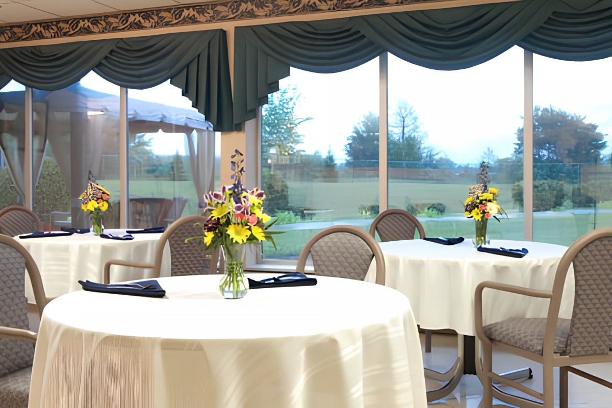 A beautifully set dining room with round tables, decorated with floral centerpieces, overlooking a scenic outdoor view.