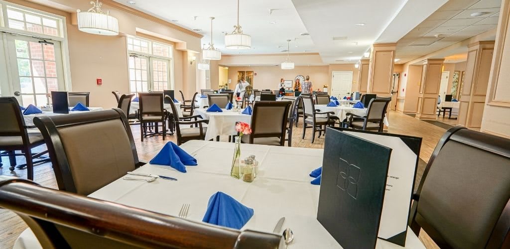 An elegant dining room with neatly arranged tables and chairs, featuring blue napkins.