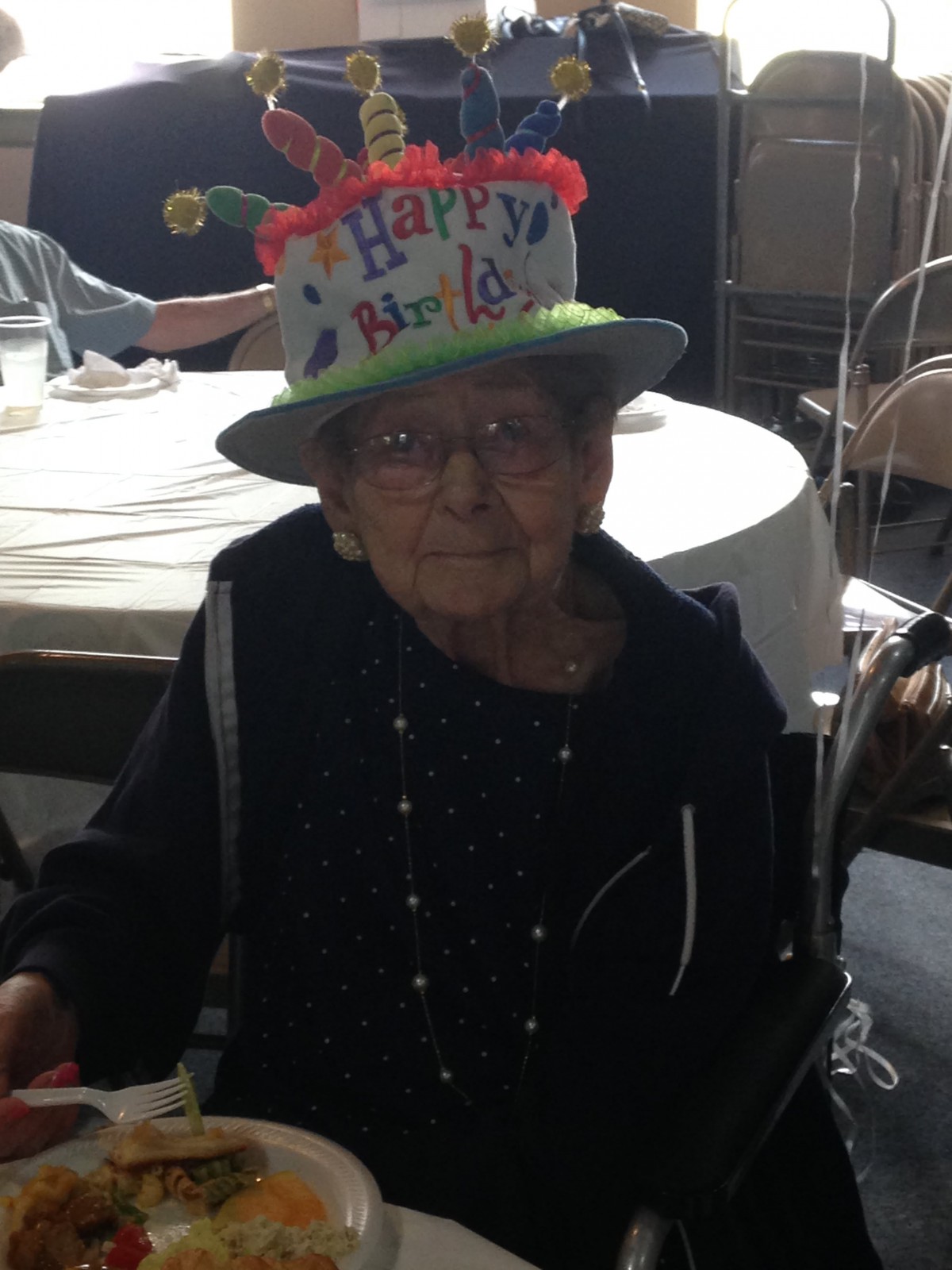 An elderly person wearing a festive 'Happy Birthday' hat indoors.
