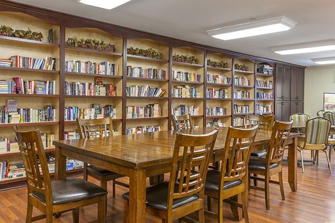 A quiet library reading room with wooden tables and chairs surrounded by bookshelves filled with books.